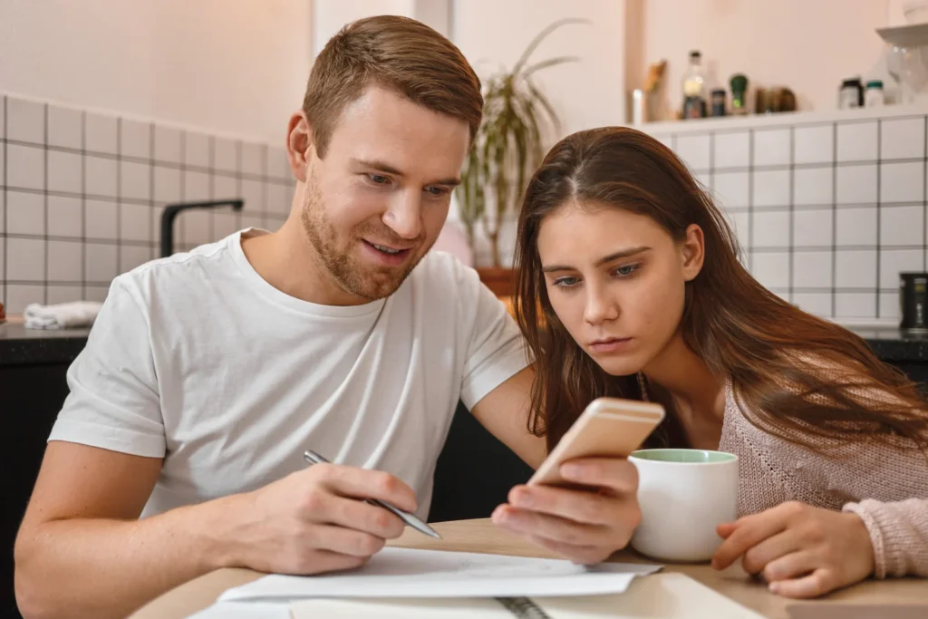 Young couple at the kitchen table checking an online loan approval on their phone