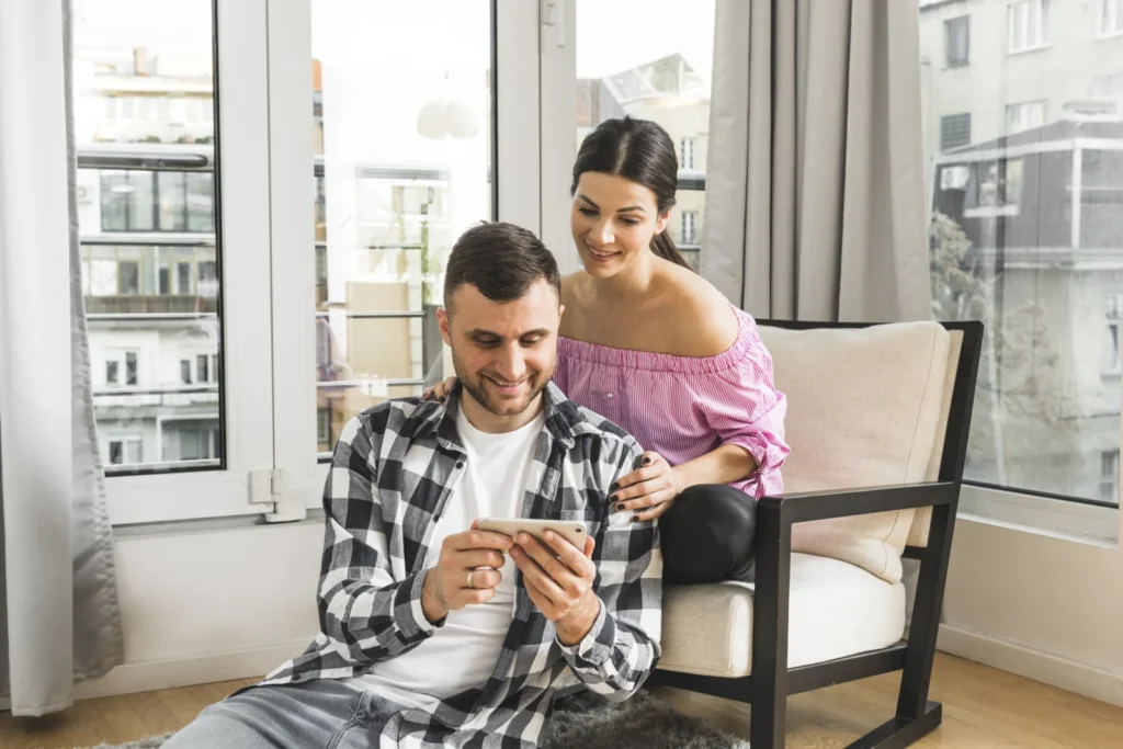 Young couple relaxing at home while one checks a mobile deposit