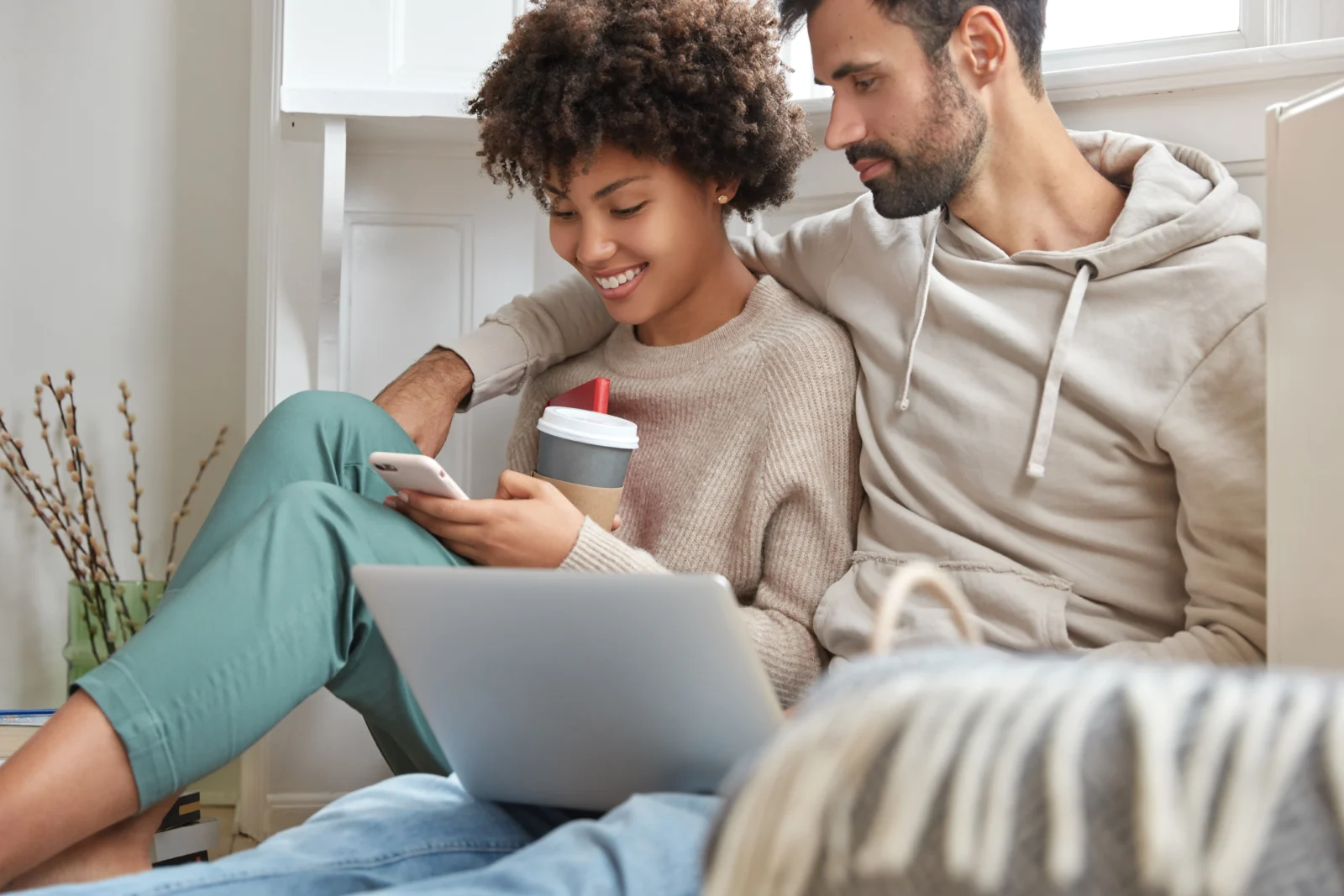 Young couple on the sofa applying online with a phone and laptop