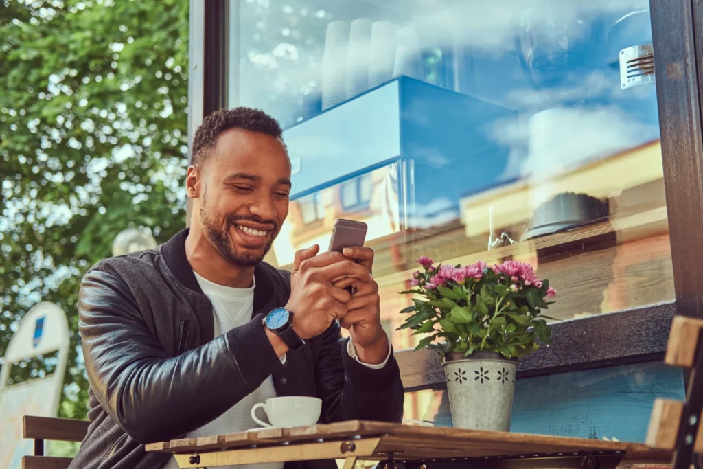 Young man smiling at his phone outside a coffee shop