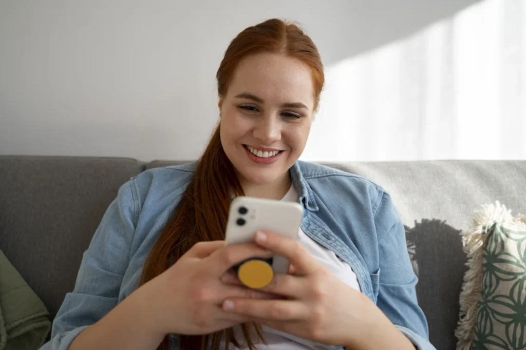 Smiling young woman on the couch checking her phone