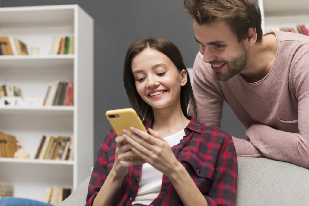 Young woman smiling at her phone with her partner beside her